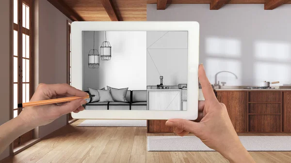Hands holding and drawing on tablet showing kitchen and living room in boho style details CAD sketch. Real finished interior in the background, architecture design presentation