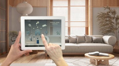 Dijital tablette akıllı uzaktan kumanda sistemi. Uygulama simgeleri olan aygıt. Japandi tarzı bir oturma odası. Koltuklar ve dekorlar, mimari iç tasarım.