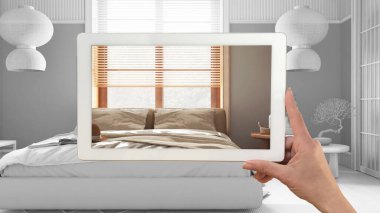 Gelişmiş gerçeklik kavramı. Özel mimari tasarımlı mobilya ürünlerini taklit etmek için kullanılan AR uygulamalı tablet, tamamen beyaz arkaplan, japandi yatak odası