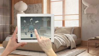Dijital tablette akıllı uzaktan kumanda sistemi. Uygulama simgeleri olan aygıt. Arka planda duvar kâğıdı, mimari iç tasarımı olan çift yataklı modern japandi yatak odası.