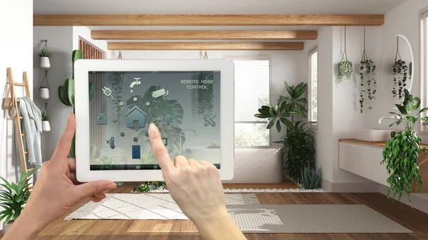 Dijital tablette akıllı uzaktan kumanda sistemi. Uygulama simgeleri olan aygıt. Küvetli modern banyo ve birçok ev bitkisi, kentsel orman iç tasarımı