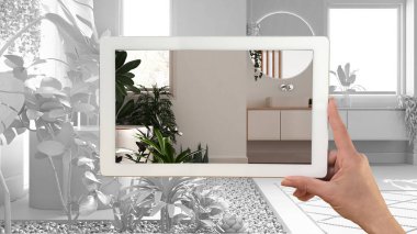 Augmented reality concept. Hand holding tablet with AR application used to simulate furniture and design products in total white unfinished background, urban jungle bathroom clipart