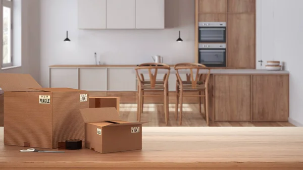 Wooden table, desk or shelf with stack of cardboard boxes over blurred view of scandinavian wooden kitchen, modern interior design, moving house concept with copy space