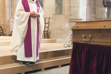 A priest in a church cassock conducts a funeral service in a French Catholic church clipart