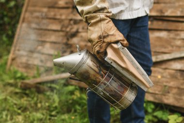 Arı yetiştiricisi arıların üzerinde arıcı tüttürüyor..