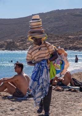Yunanistan, Mykonos, Ağustos 2024: Yunanistan 'ın Mykonos adasının sahilinde bir plaj şapka ve aksesuar satıcısı