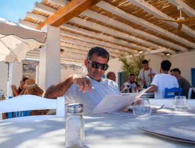Mykonos, Yunanistan. Ağustos 2024: Yunanistan 'ın Mykonos adasındaki bir tavernada bir adam menüyü okuyor
