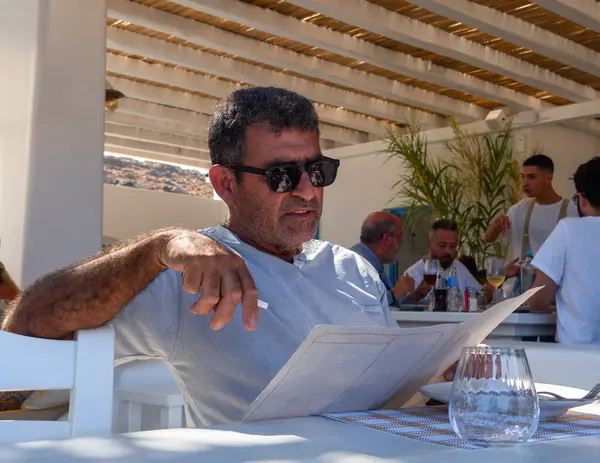 Mykonos, Yunanistan. Ağustos 2024: Yunanistan 'ın Mykonos adasındaki bir tavernada bir adam menüyü okuyor