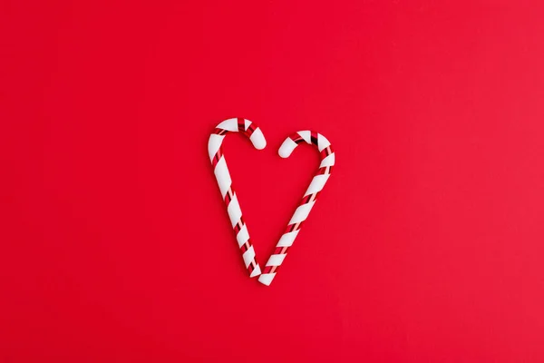 Heart from candy cane on a red  background. Creative minimal christmas art