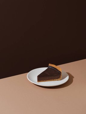 Piece of drk chocolate cheesecake on beige and brown background. Minimalist food photography