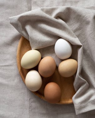 Nature colors Easter eggs. Eggs on a wooden plate on a beige napkin. A chicken egg as a valuable nutritious product. Top view flat lay 