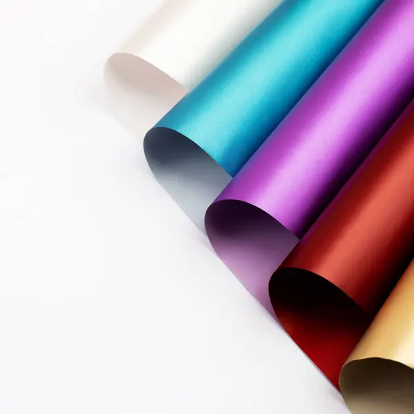 Different colorful wrapping paper rolls on white background, close up. Rolls of deep rich colors wrapping paper
