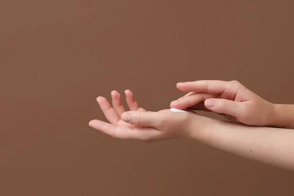 Beautiful young woman hands with cream. Woman applies cream on her hands with nice natural short nails on brown background