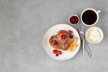 Gri arka planda Sevgililer Günü kahvaltısı. Beyaz tabakta tereyağlı ve dutlu çörek ve bir fincan kahve. Üst görünüm, alanı kopyala