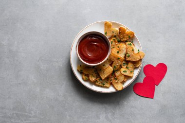 Sevgililer Günü kızarmış patates kalplerini beyaz bir tabakta, beton zemin üzerinde kırmızı kağıt kalplerle. Sevgililer Günü için romantik yemek fikirleri, üst manzara