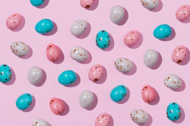Pembe arka planda bej, pembe ve mavi renkte çikolatalı Paskalya yumurtaları. Yaratıcı Paskalya konsepti, üst görünüm