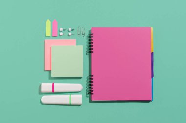 Not defteri, fosforlu kalem, açık yeşil arka planda raptiye ve kağıt çarşaflar. Açık yeşil arka planda ofis ve okul malzemeleri. Okul konseptine geri dön, üst görünüm