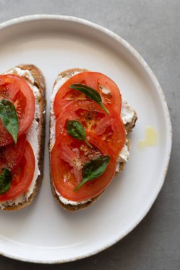 Krem peynirli kahvaltı tostları, taze domates, zeytinyağı ve beyaz tabakta bebek ıspanağı. Sağlıklı lezzetli yiyecek konsepti, üst görünüm, kopyalama alanı
