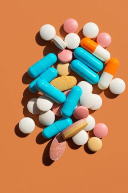 Kahverengi arka planda bir sürü hap ve tablet var. Mavi, pembe, sarı ve beyaz. Yaratıcı tabletler konsepti, üst görünüm