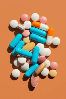 Kahverengi arka planda bir sürü hap ve tablet var. Mavi, pembe, sarı ve beyaz. Yaratıcı tabletler konsepti, üst görünüm