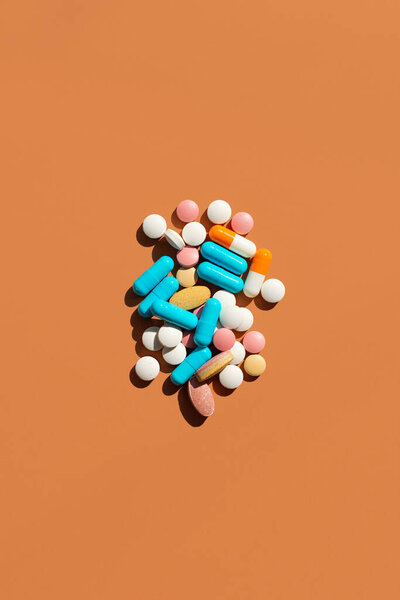 Lots of pills and tablets blue, pink, yellow and white colors on brown background. Creative tablets concept, top view