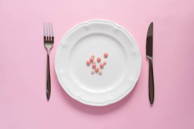 Pembe arka planda beyaz bir tabletteki pembe yuvarlak tabletlerin üst görüntüsü. Yaratıcı haplar konsepti, kopyalama alanı