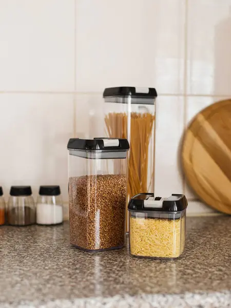 Mutfak masasında spagetti, makarna ve mısır gevreğiyle dolu hava geçirmez şeffaf yiyecek kapları. Gevşek ürünler için organizatörler, mutfakta yer düzenleme