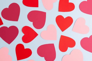 Pastel mavi arka planda çeşitli boyutlarda kırmızı ve pembe kağıt kalpler var. Sevgililer Günü, aşk ve duygular konsepti, üst görünüm