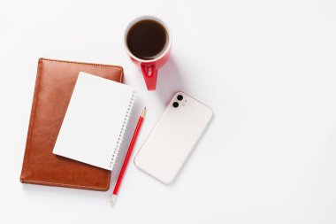 Kahverengi defter, kırmızı kalem, beyaz akıllı telefon ve beyaz zemin üzerinde kahve olan kırmızı bardak. Gün için sabah planları, çalışma alanı. Üretkenlik ve konsantrasyon konsepti, üst görünüm
