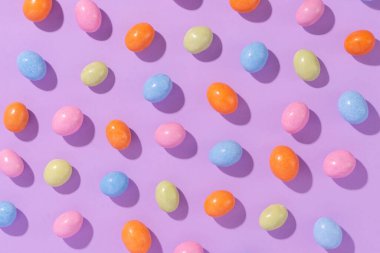 Menekşe arka planında renkli bir paskalya süprüntüsü. Cilalı yumurta şeklinde rengarenk şekerler. Yaratıcı paskalya konsepti, üst görünüm