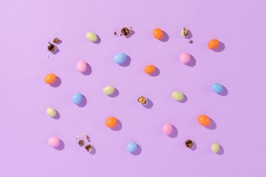 Menekşe arka planında renkli bir paskalya süprüntüsü. Cilalı yumurta şeklinde rengarenk şekerler. Yaratıcı paskalya konsepti, üst görünüm