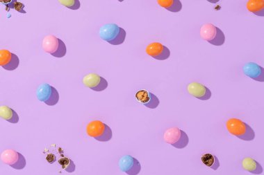 Menekşe arka planında renkli bir paskalya süprüntüsü. Cilalı yumurta şeklinde rengarenk şekerler. Yaratıcı paskalya konsepti, üst görünüm