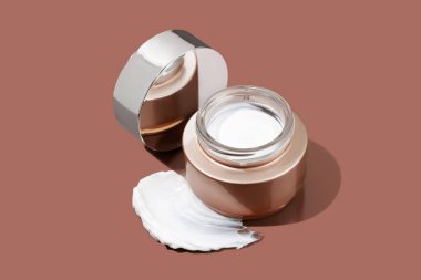 Yüz kremi ya da kahverengi arka planda beyaz krem desenli el kremi şişesi. Krema ya da losyon için kahverengi şişe. Cilt bakımı ya da güneş kremi. Güzellik konsepti, boşluğu kopyala