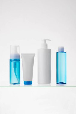 Beyaz arka planda cam bir rafta farklı kozmetik ürünler. Cam bir rafta cilt bakımı ve banyo ürünleri. Güzellik ürünleri içeren dağıtıcılar ve tüpler, boşluğu kopyala