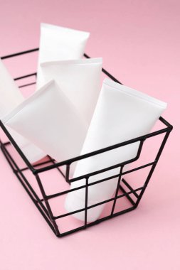 Pembe arka planda siyah sepetli beyaz plastik tüpün yaratıcı fotoğrafı. Cilt ürünleri, kozmetik fotoğrafçılığı