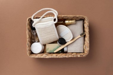 Banyo aletlerinin ve organik kozmetik ürünlerinin kahverengi arka planda doğal, çevre dostu güzellik gereksinimlerini ve kişisel bakım rutin konseptini vurgulayan dokuma sepetindeki üst görünümü. Doğal cilt bakımı ve sağlıklı yaşam ürünleri.