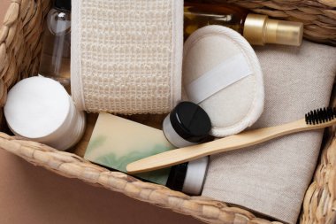 Banyo aletlerinin ve organik kozmetik ürünlerinin kahverengi arka planda doğal, çevre dostu güzellik gereksinimlerini ve kişisel bakım rutin konseptini vurgulayan dokuma sepetindeki üst görünümü. Doğal cilt bakımı ve sağlıklı yaşam ürünleri.