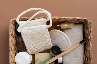 Banyo aletlerinin ve organik kozmetik ürünlerinin kahverengi arka planda doğal, çevre dostu güzellik gereksinimlerini ve kişisel bakım rutin konseptini vurgulayan dokuma sepetindeki üst görünümü. Doğal cilt bakımı ve sağlıklı yaşam ürünleri.