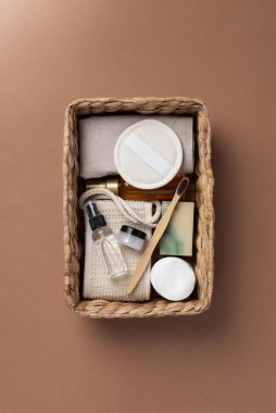 Banyo aletlerinin ve organik kozmetik ürünlerinin kahverengi arka planda doğal, çevre dostu güzellik gereksinimlerini ve kişisel bakım rutin konseptini vurgulayan dokuma sepetindeki üst görünümü. Doğal cilt bakımı ve sağlıklı yaşam ürünleri.