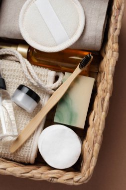 Banyo aletlerinin ve organik kozmetik ürünlerinin kahverengi arka planda doğal, çevre dostu güzellik gereksinimlerini ve kişisel bakım rutin konseptini vurgulayan dokuma sepetindeki üst görünümü. Doğal cilt bakımı ve sağlıklı yaşam ürünleri.