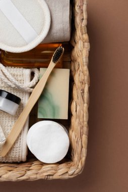 Banyo aletlerinin ve organik kozmetik ürünlerinin kahverengi arka planda doğal, çevre dostu güzellik gereksinimlerini ve kişisel bakım rutin konseptini vurgulayan dokuma sepetindeki üst görünümü. Doğal cilt bakımı ve sağlıklı yaşam ürünleri.