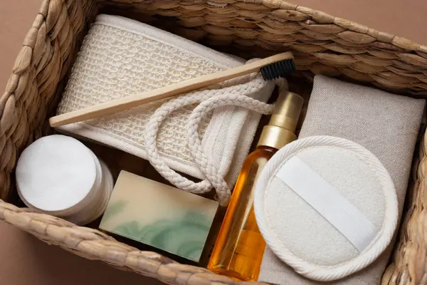 Banyo aletlerinin ve organik kozmetik ürünlerinin kahverengi arka planda doğal, çevre dostu güzellik gereksinimlerini ve kişisel bakım rutin konseptini vurgulayan dokuma sepetindeki üst görünümü. Doğal cilt bakımı ve sağlıklı yaşam ürünleri.