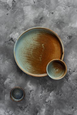 Yuvarlak bir plaka, gri beton arka planda sıcak renklerde bir kenarı var. Yumuşak renk paletinde doğal elementlerle minimalist kompozisyon. El yapımı ahenk konsepti, üst görünüm