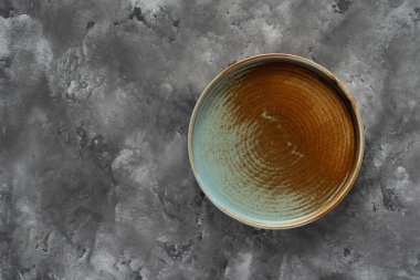 Yuvarlak bir plaka, gri beton arka planda sıcak renklerde bir kenarı var. Yumuşak renk paletinde doğal elementlerle minimalist kompozisyon. El yapımı ahenk konsepti, üst görünüm