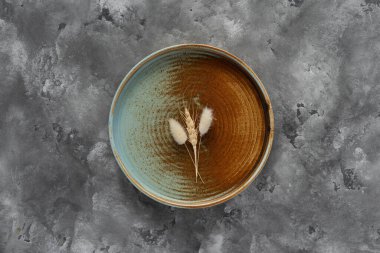 Yuvarlak bir plaka, gri beton arka planda sıcak renklerde bir kenarı var. Yumuşak renk paletinde doğal elementlerle minimalist kompozisyon. El yapımı ahenk konsepti, üst görünüm
