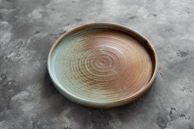 Yuvarlak bir plaka, gri beton arka planda sıcak renklerde bir kenarı var. Yumuşak renk paletinde doğal elementlerle minimalist kompozisyon. El yapımı ahenk konsepti, üst görünüm