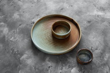 Yuvarlak bir plaka, gri beton arka planda sıcak renklerde bir kenarı var. Yumuşak renk paletinde doğal elementlerle minimalist kompozisyon. El yapımı ahenk konsepti, üst görünüm