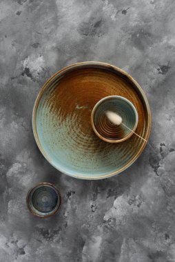 Yuvarlak bir plaka, gri beton arka planda sıcak renklerde bir kenarı var. Yumuşak renk paletinde doğal elementlerle minimalist kompozisyon. El yapımı ahenk konsepti, üst görünüm