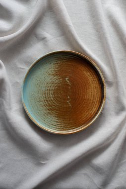 Yuvarlak plaka, bej rengi pamuk masa örtüsünün üzerinde sıcak renklerde bir kenarı var. Yumuşak renk paletinde doğal elementlerle minimalist kompozisyon. El yapımı ahenk konsepti, üst görünüm