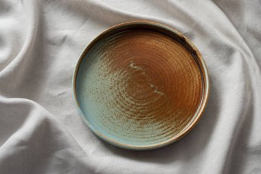 Yuvarlak plaka, bej rengi pamuk masa örtüsünün üzerinde sıcak renklerde bir kenarı var. Yumuşak renk paletinde doğal elementlerle minimalist kompozisyon. El yapımı ahenk konsepti, üst görünüm